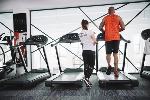 Back view of personal trainer supervising african american sportsman running on treadmill — Stock Photo
