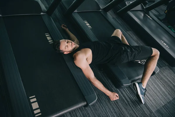 Top view of unconscious sportsman lying on treadmill in gym — Stock Photo