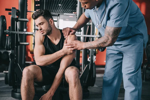 Attentif afro-américain médecin toucher l'épaule blessée du jeune sportif — Photo de stock