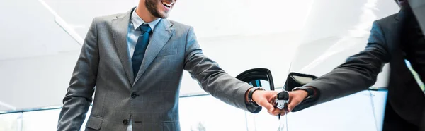 Panoramic shot of happy man in suit opening car door in car showroom — Stock Photo