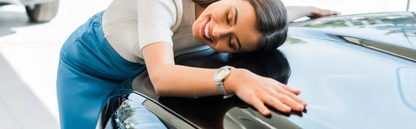 Tiro panorámico de chica feliz con los ojos cerrados cerca de coche negro - foto de stock