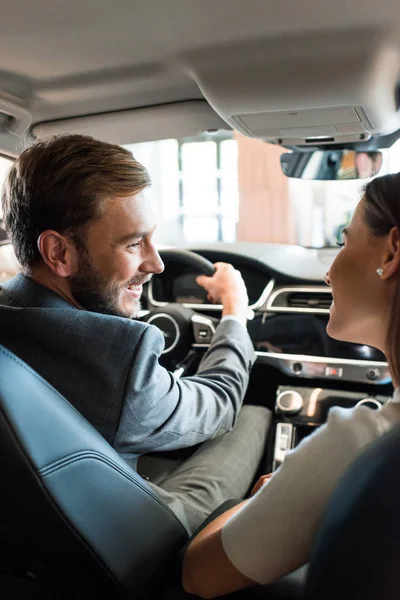 Enfoque selectivo de hombre barbudo feliz sosteniendo el volante y mirando a la mujer en el coche - foto de stock