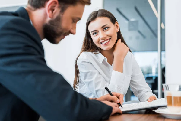 Selective focus of cheerful car dealer looking at man holding pen — Stock Photo