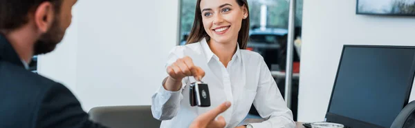 Panoramic shot of cheerful car dealer giving car key to man — Stock Photo