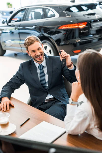 Selective focus of cheerful bearded car dealer holding car keys near woman — Stock Photo