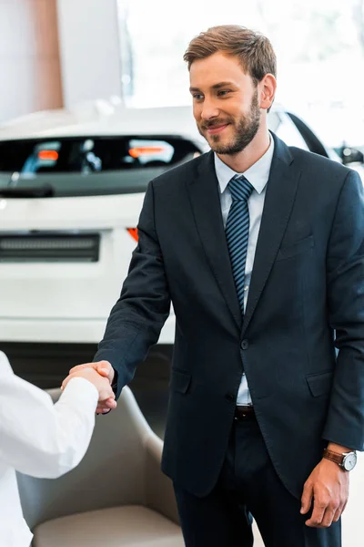Cropped view of woman shaking hands with happy car dealer in car showroom — Stock Photo