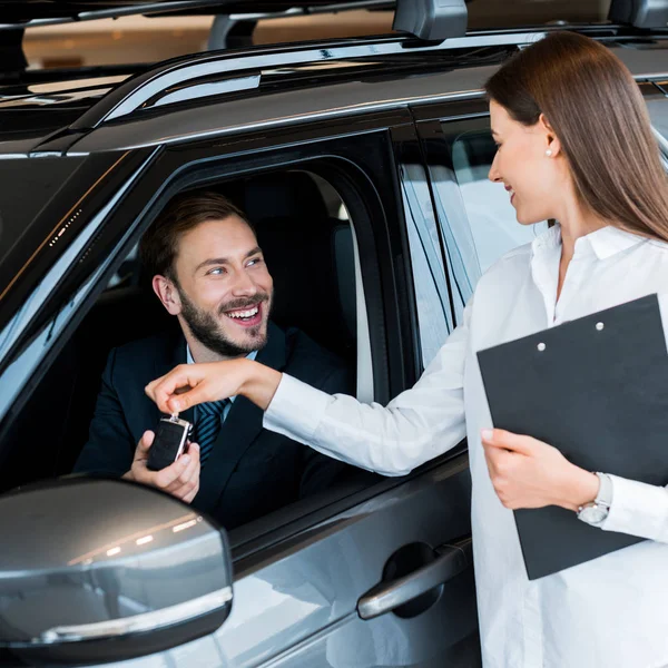 Selektiver Fokus der attraktiven Frau, die dem glücklichen Mann im Auto den Autoschlüssel gibt — Stockfoto