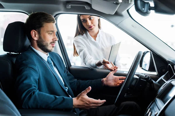 Attraktive Frau sieht gutaussehenden bärtigen Mann gestikulierend im Auto sitzend an — Stockfoto