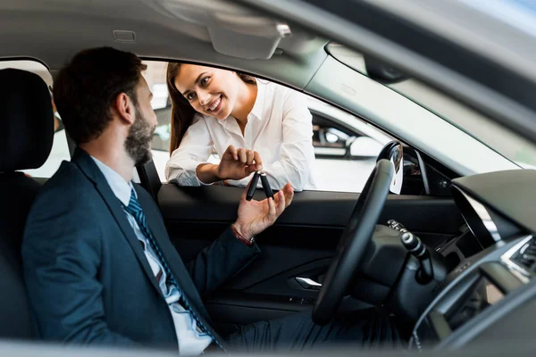 Selektiver Fokus der fröhlichen Frau, die dem bärtigen Mann im Auto den Autoschlüssel gibt — Stockfoto
