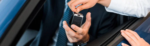 Panoramic shot of woman giving car key to man in car — Stock Photo