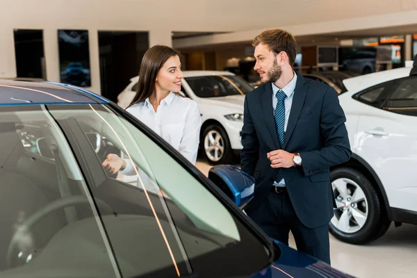 Messa a fuoco selettiva di allegro concessionario di auto gesticolando mentre guardando l'uomo barbuto in auto showroom — Foto stock