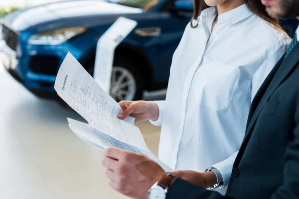 Vue recadrée de la femme et l'homme tenant des papiers avec lettrage dans la salle d'exposition de voiture — Photo de stock