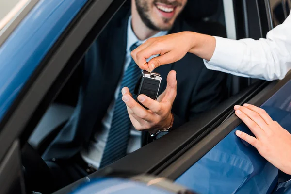 Visão cortada do carro concessionário dando a chave do carro para o homem barbudo — Fotografia de Stock