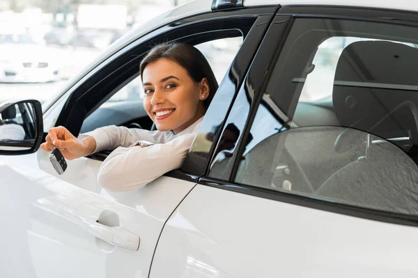 Joyeuse jeune femme tenant clé de voiture tout en étant assis dans la voiture — Photo de stock