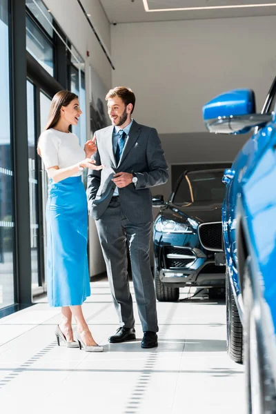 Mujer alegre gesto de pie y mirando hombre barbudo guapo cerca de los coches - foto de stock