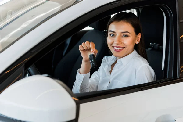 Foyer sélectif de la femme heureuse tenant la clé de voiture tout en étant assis dans la voiture — Photo de stock