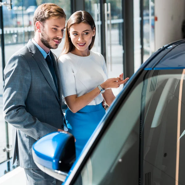 Foco seletivo da mulher bonita gesticulando enquanto está de pé com homem bonito e carro azul — Fotografia de Stock