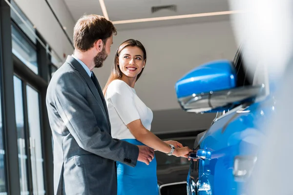 Uomo barbuto in piedi con donna attraente vicino auto blu — Foto stock