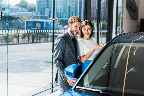 Selective focus of beautiful girl gesturing while standing with handsome man and blue car — Stock Photo