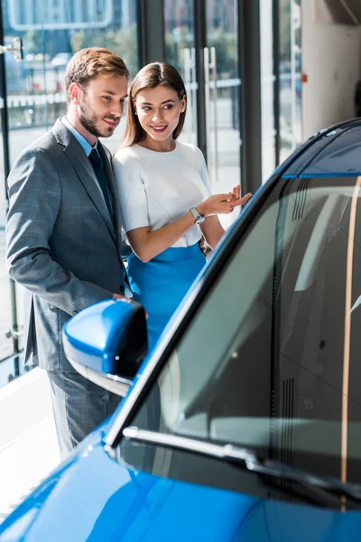 Selective focus of beautiful girl gesturing while standing with handsome man in suit and blue car — Stock Photo