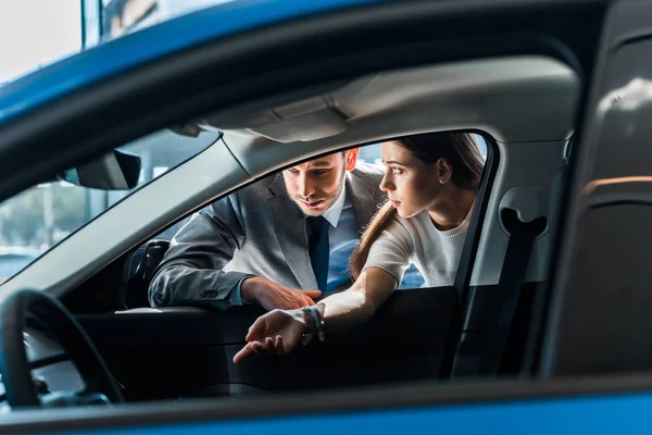 Foyer sélectif de bel homme près de la femme attrayante et l'automobile dans la salle d'exposition de voiture — Photo de stock