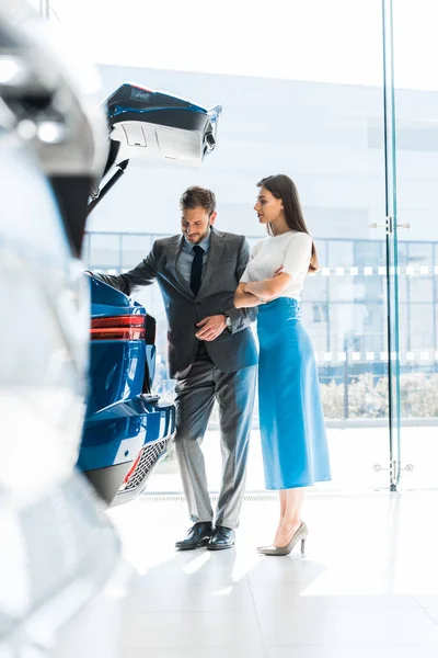 Selektiver Fokus glücklicher Frauen und Männer beim Blick auf den Kofferraum im Autohaus — Stockfoto