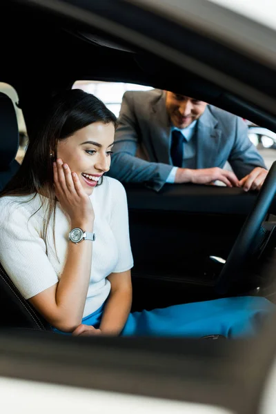 Вибірковий фокус збудженої дівчини, що сидить в машині біля бородатого чоловіка в автосалоні — стокове фото