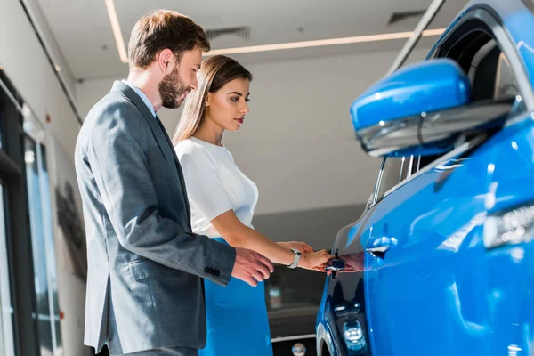 Селективное внимание красивой женщины, стоящей рядом с мужчиной и синей машиной — стоковое фото