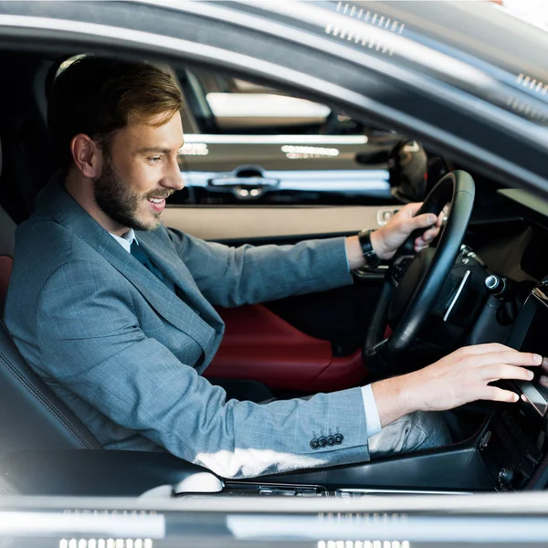 Selective focus of cheerful bearded driver sitting on car and touching display — Stock Photo
