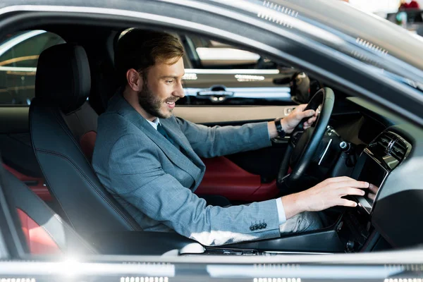 Selektiver Fokus des glücklichen bärtigen Fahrers, der auf dem Auto sitzt und das Display berührt — Stockfoto