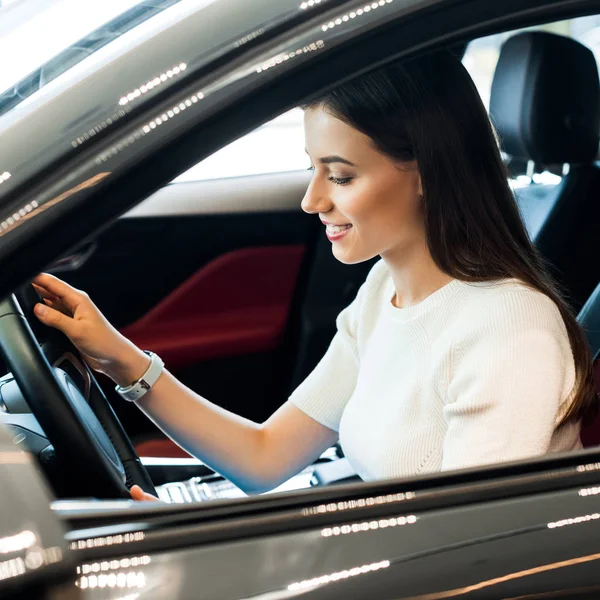 Messa a fuoco selettiva di donna felice toccando volante mentre seduto in auto — Foto stock
