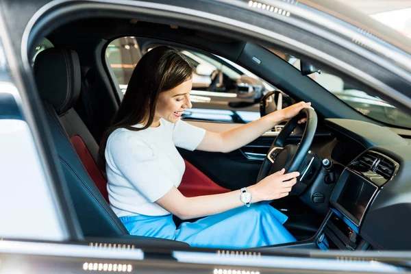 Selektiver Fokus einer lächelnden Frau, die im Auto sitzt und das Lenkrad berührt — Stockfoto