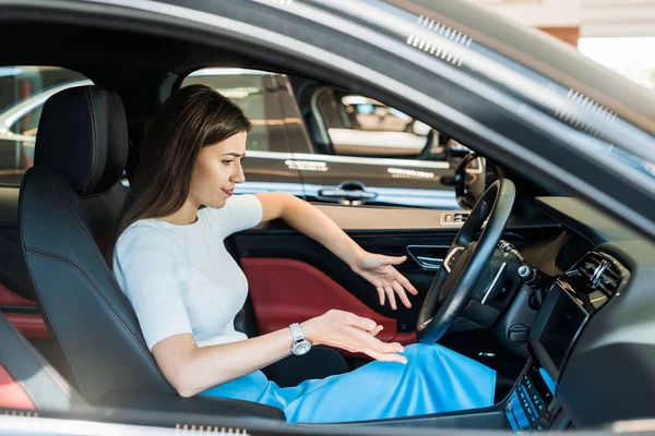 Confused woman gesturing while sitting in modern car — Stock Photo
