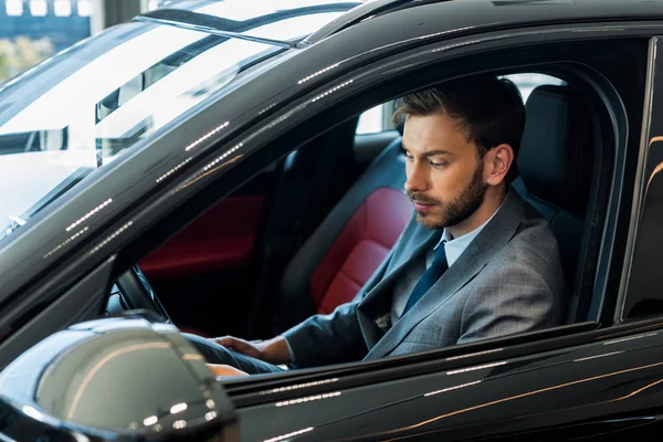 Selektiver Fokus eines gutaussehenden bärtigen Mannes, der auf einem modernen Auto sitzt — Stockfoto