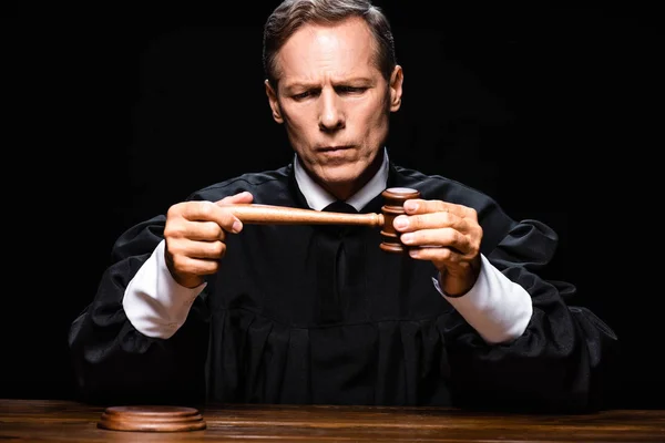 Суддя в судовому халаті, сидячи за столом і тримаючи данину ізольованою на чорному — стокове фото