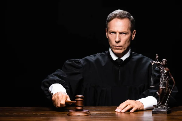 Judge in judicial robe sitting at table and hit with gavel isolated on black — Stock Photo
