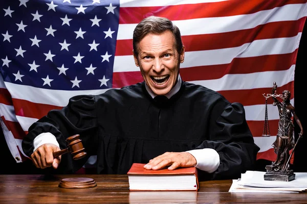 Angry judge in judicial robe hitting gavel and putting hand on book — Stock Photo
