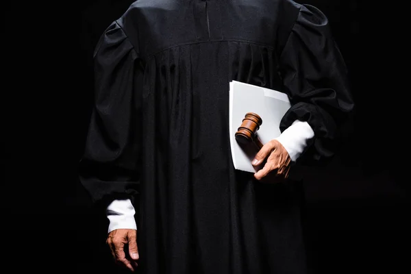 Vista recortada del juez en bata judicial sosteniendo mazo y papeles aislados en negro - foto de stock