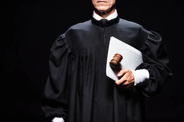 Vista recortada del juez en bata judicial sosteniendo mazo y papeles aislados en negro - foto de stock