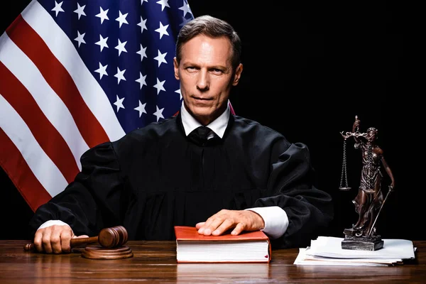 Judge in judicial robe holding gavel and putting hand on book — Stock Photo