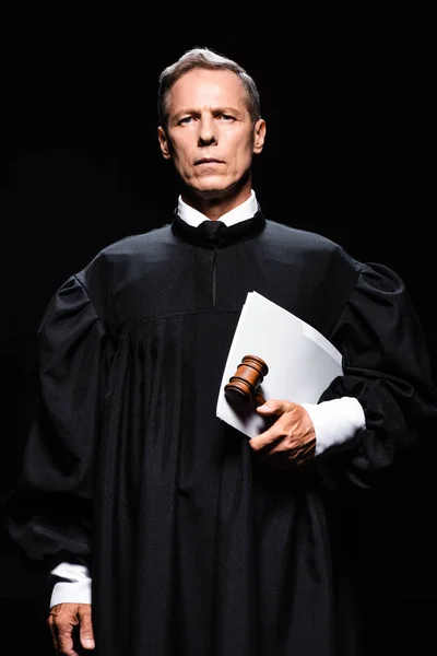 Judge in judicial robe holding gavel and papers isolated on black — Stock Photo