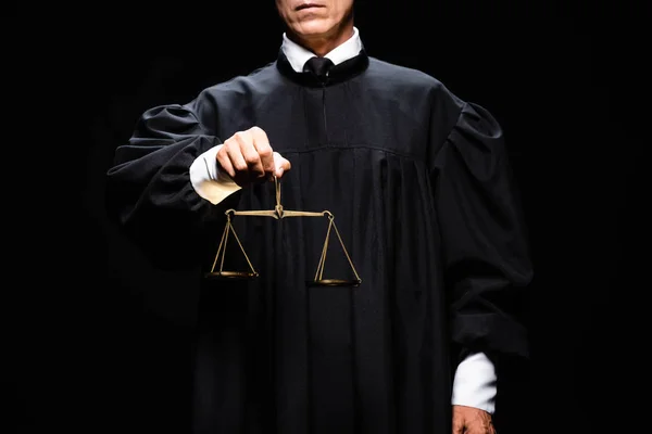 Обрізаний погляд судді в судовому халаті, що тримає ваги правосуддя ізольовані на чорному — стокове фото