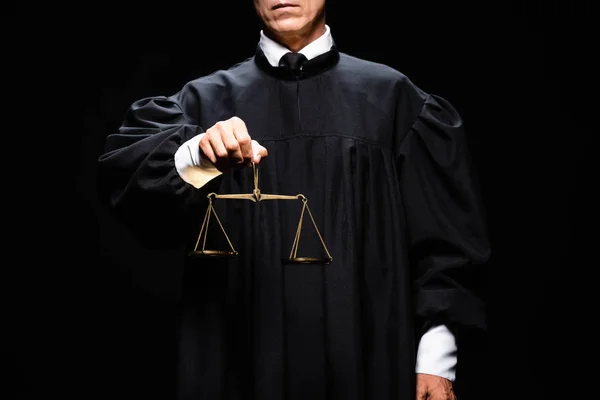 Cropped view of judge in judicial robe holding scales of justice isolated on black — Stock Photo