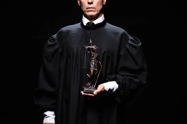 Cropped view of judge in judicial robe holding themis figure isolated on black — Stock Photo