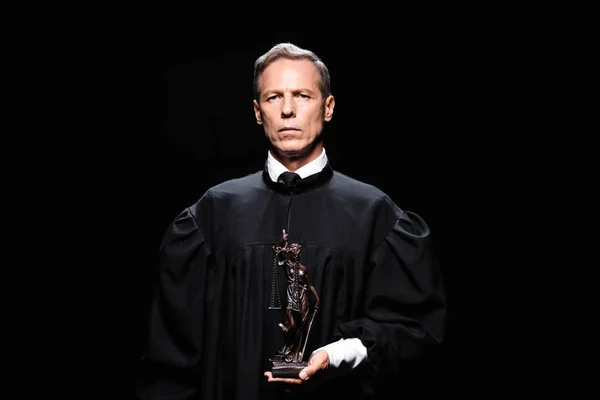 Judge in judicial robe holding themis figure isolated on black — Stock Photo