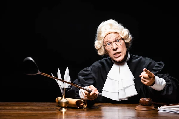 Angry judge in judicial robe and wig holding golf club and pointing with finger isolated on black — Stock Photo