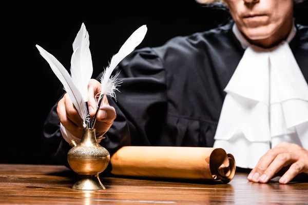 Cropped view of judge in judicial robe taking feather isolated on black — Stock Photo