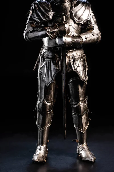 Cropped view of knight in armor holding sword on black background — Stock Photo