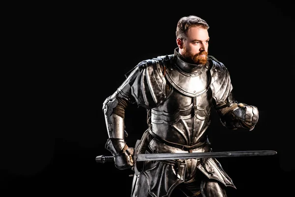 Красивий лицар в обладунках, що тримає меч ізольовано на чорному — стокове фото