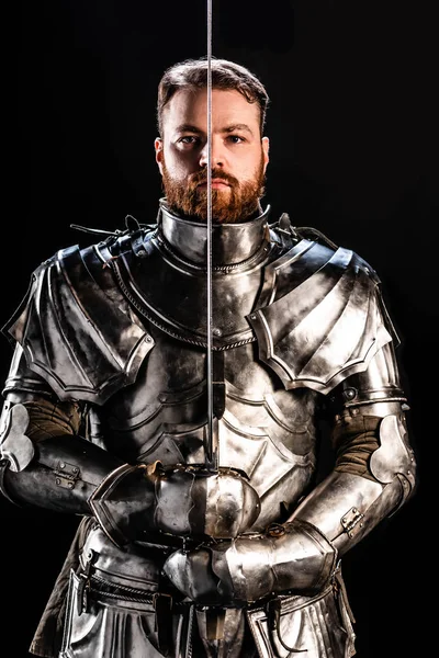 Handsome knight in armor holding sword isolated on black — Stock Photo